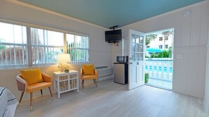 A room with a TV, two chairs, a small table, and a door leading to a pool area. - The Islander Inn (Vero Beach)