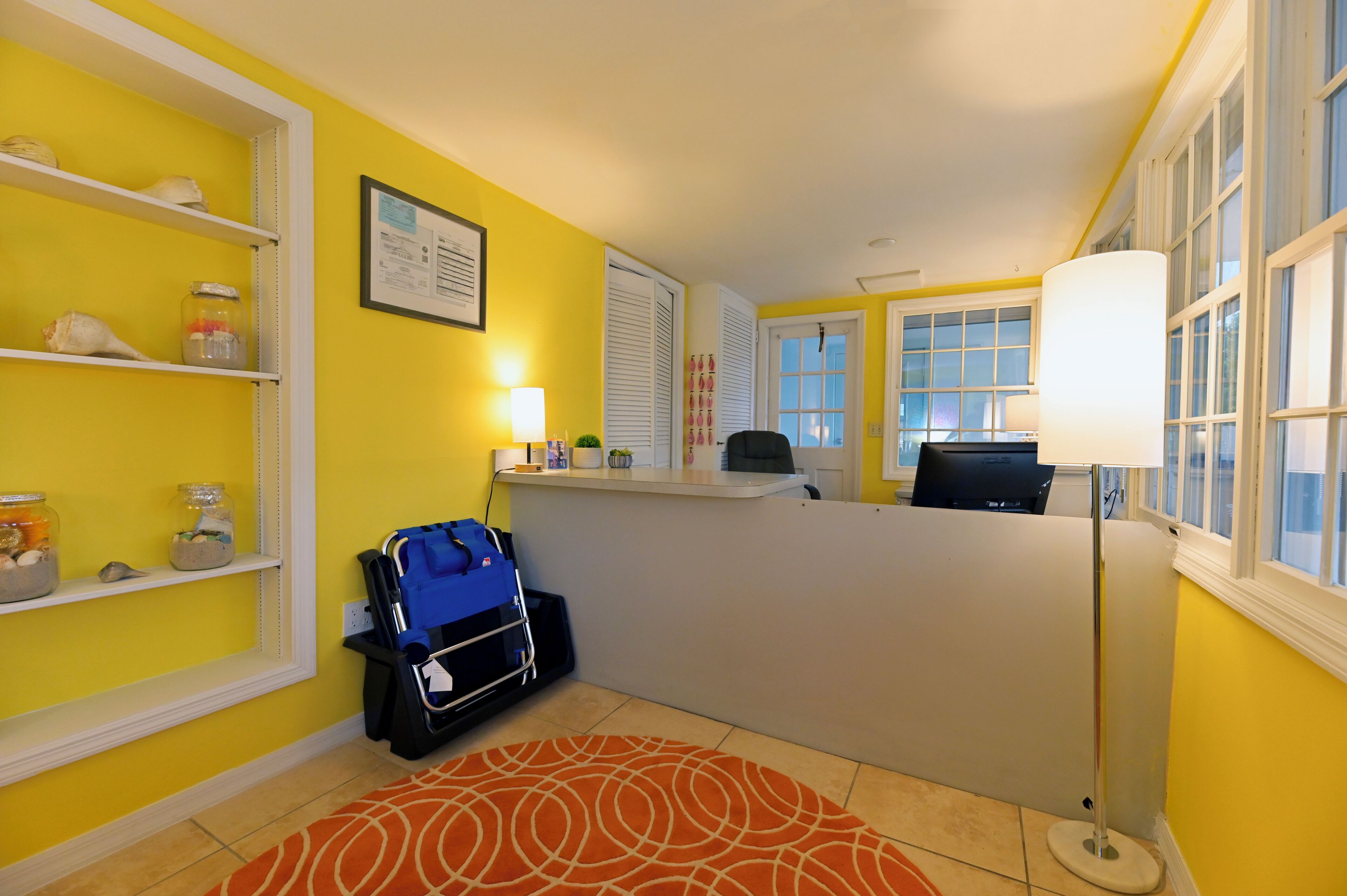 A reception area with a desk, a blue bag, shelves with jars, and a patterned rug.