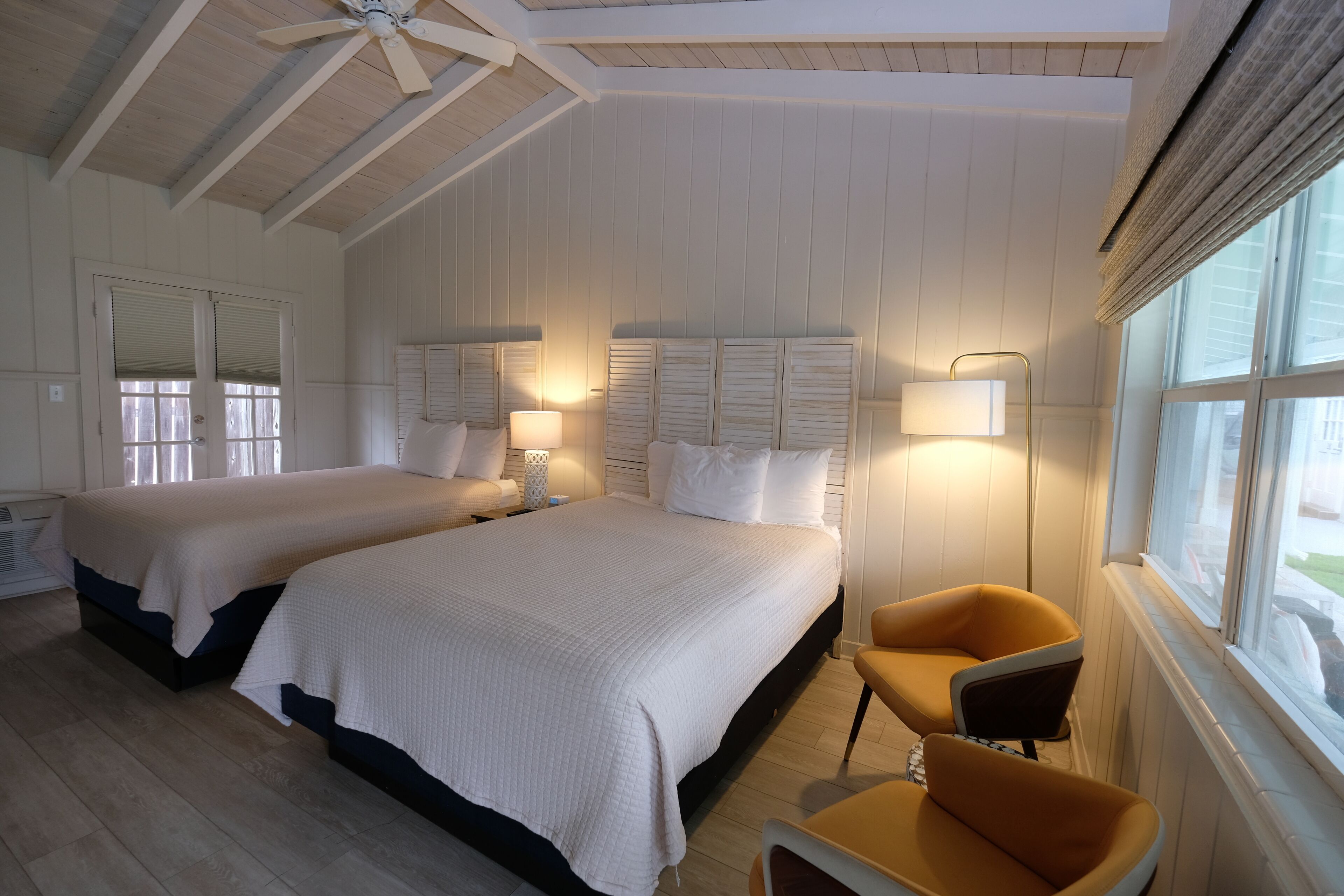 Ett hotellrum med två sängar, ett fönster med gardiner, en takfläkt och en stol.