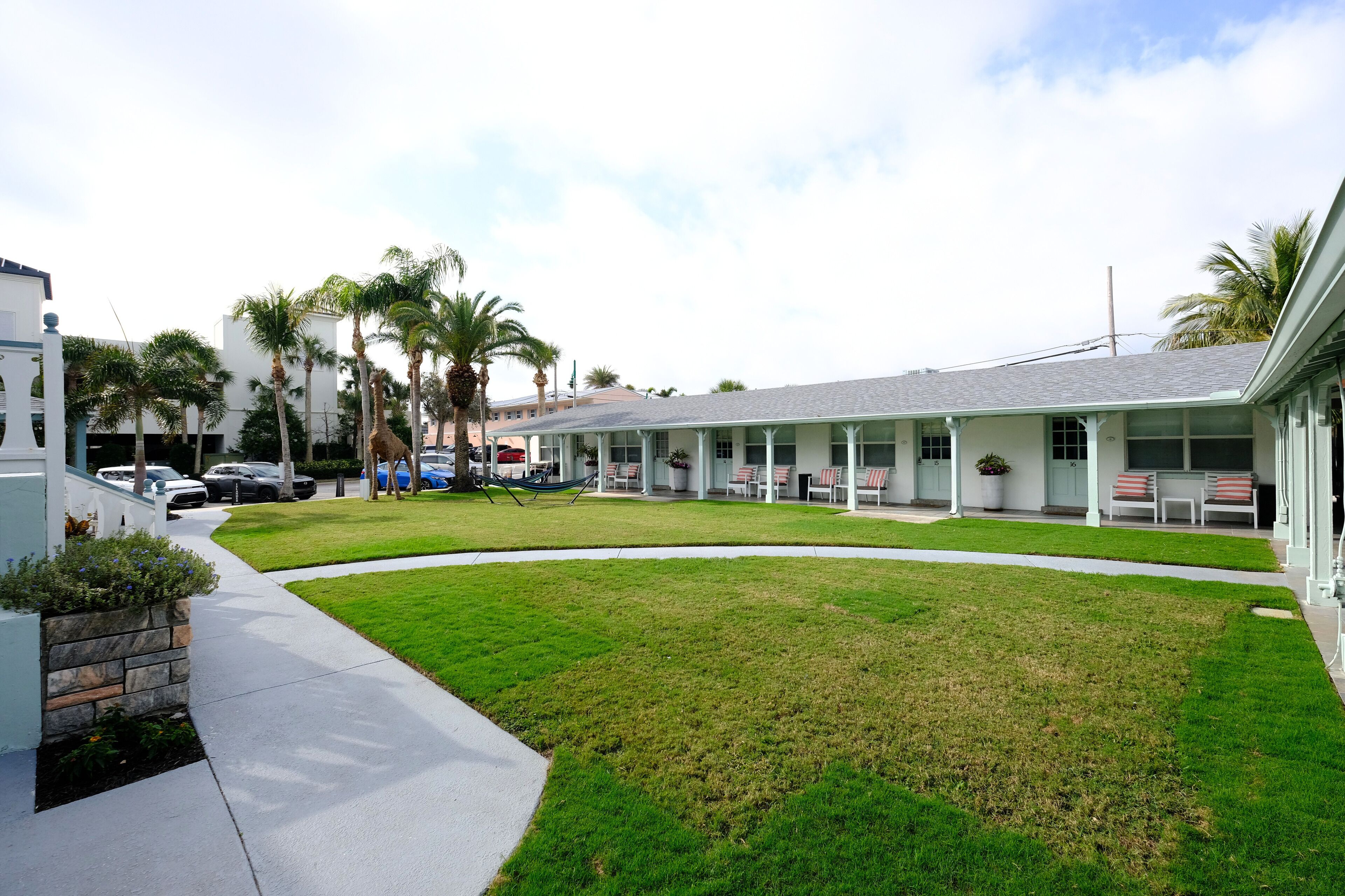 Un motel con césped, palmeras y una hilera de habitaciones con asientos al aire libre.