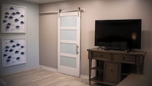 A room with a sliding door, a flat-screen TV on a wooden stand, and two framed fish artwork on the wall. - The Islander Inn (Vero Beach)