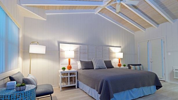 A bedroom with a large bed, two bedside tables with lamps, a chair, and a small side table with a plant. - The Islander Inn (Vero Beach)