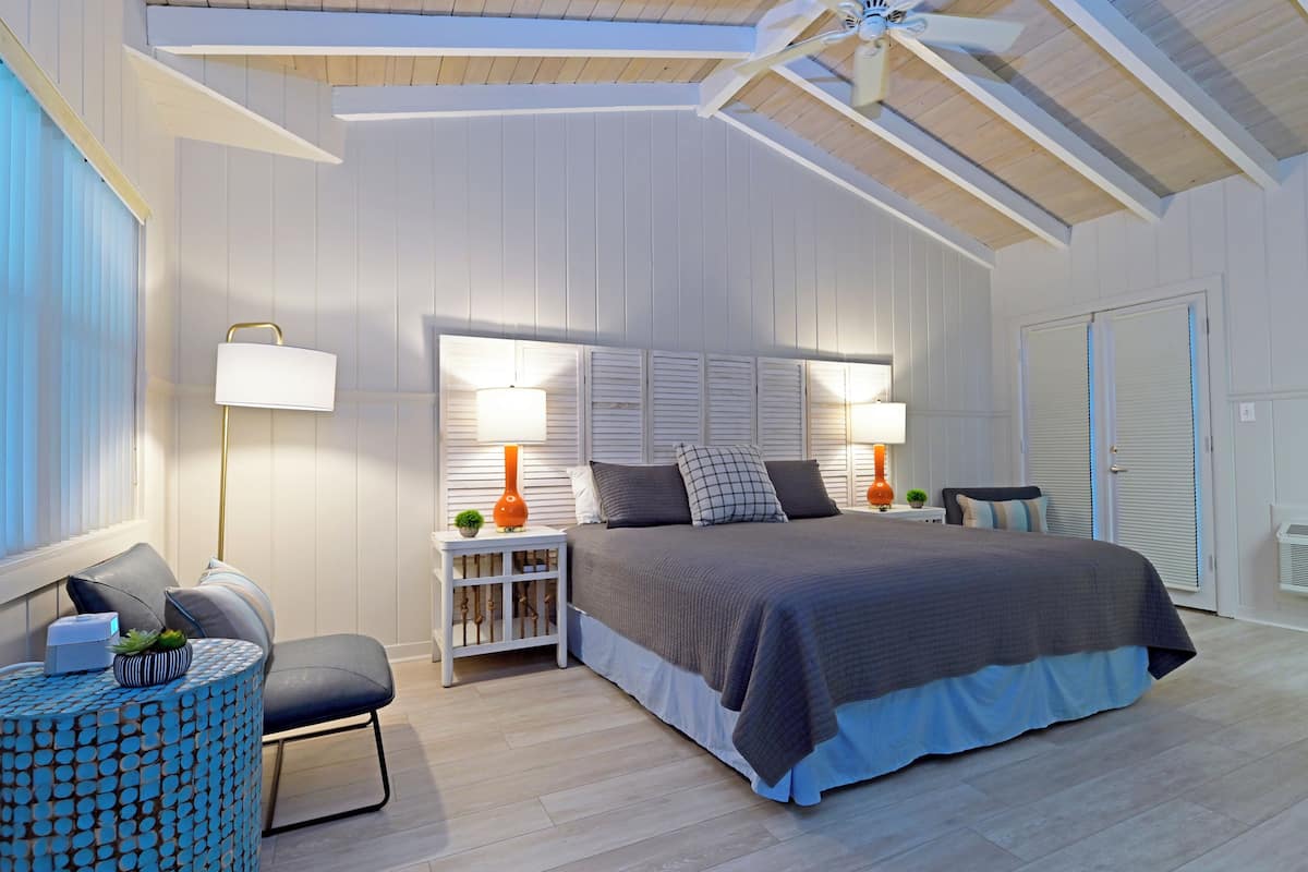 A bedroom with a large bed, two bedside tables with lamps, a chair, and a small side table with a plant.