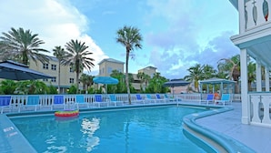 A pool area with lounge chairs and umbrellas, surrounded by palm trees and buildings. - The Islander Inn (Vero Beach)