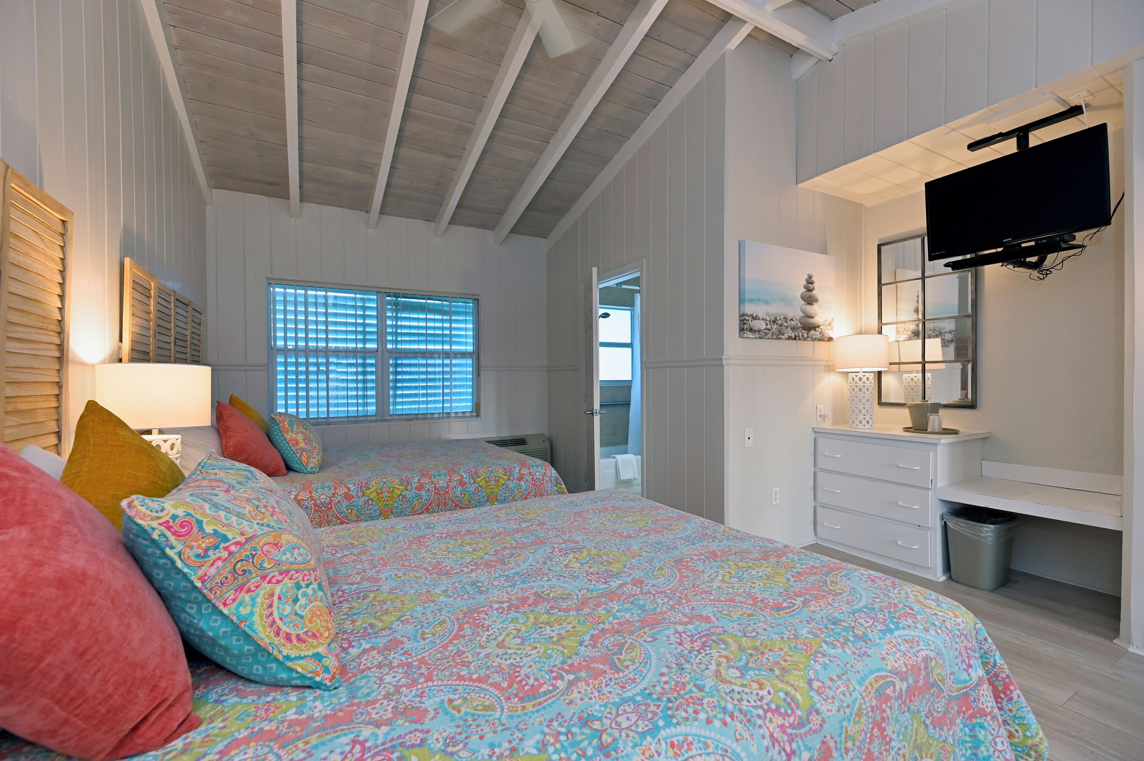 Un dormitorio con dos camas, televisión, cómoda y ventana con persianas.