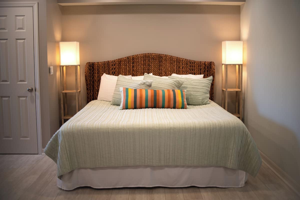 A neatly made bed with a striped bedspread and multiple pillows, flanked by two bedside lamps on either side.