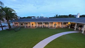 A hotel with a covered outdoor seating area, a palm tree, and a white pathway. - The Islander Inn (Vero Beach)
