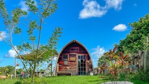 A rustic barn-style building with a red facade, surrounded by a grassy yard and trees. - Chalé e Suítes Naldiane (Mata de São João)