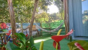 A garden with artificial grass, a hammock, and a mural of a giraffe and a leopard. - Chalé e Suítes Naldiane (Mata de São João)