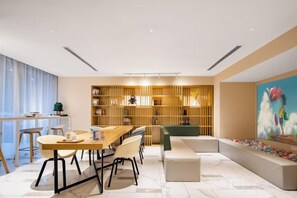 A modern interior with a dining area, a bookshelf, and a colorful painting. - Magnotel Classic (Changchun Convention and Exhibition Center) (Changchun)