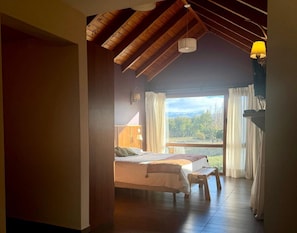 A bedroom with a bed, a window with curtains, a wooden ceiling, and a nightstand.
