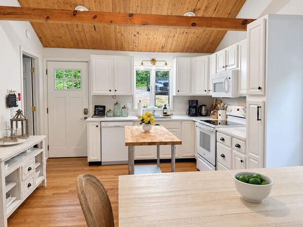A modern kitchen with white cabinetry, a wooden ceiling, and a dining area with a table and chairs.
