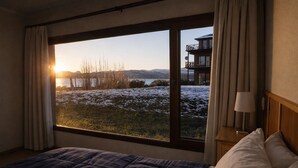 Quarto com uma grande janela que oferece vista para uma paisagem nevada e um edifício à distância, sobre a água.