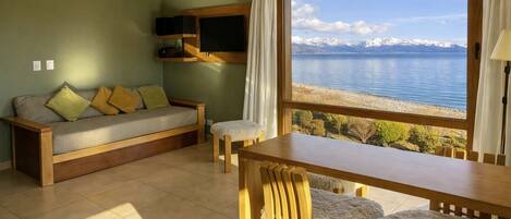 A room with a sofa, a table, and a view of a lake and mountains.