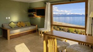 Una habitación con sofá, una mesa y vistas a un lago y montañas.