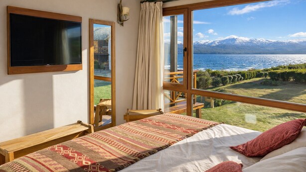 A bedroom with a bed, a TV, and a view of a lake and mountains. - Nahuel Superior "North" (Dina Huapi)