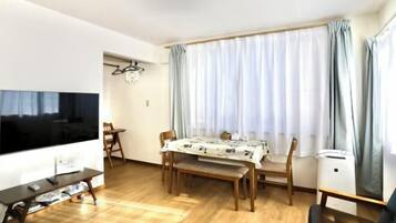 Un salon comprenant une table à manger en bois, des chaises, un banc, un téléviseur et une fenêtre avec des rideaux.