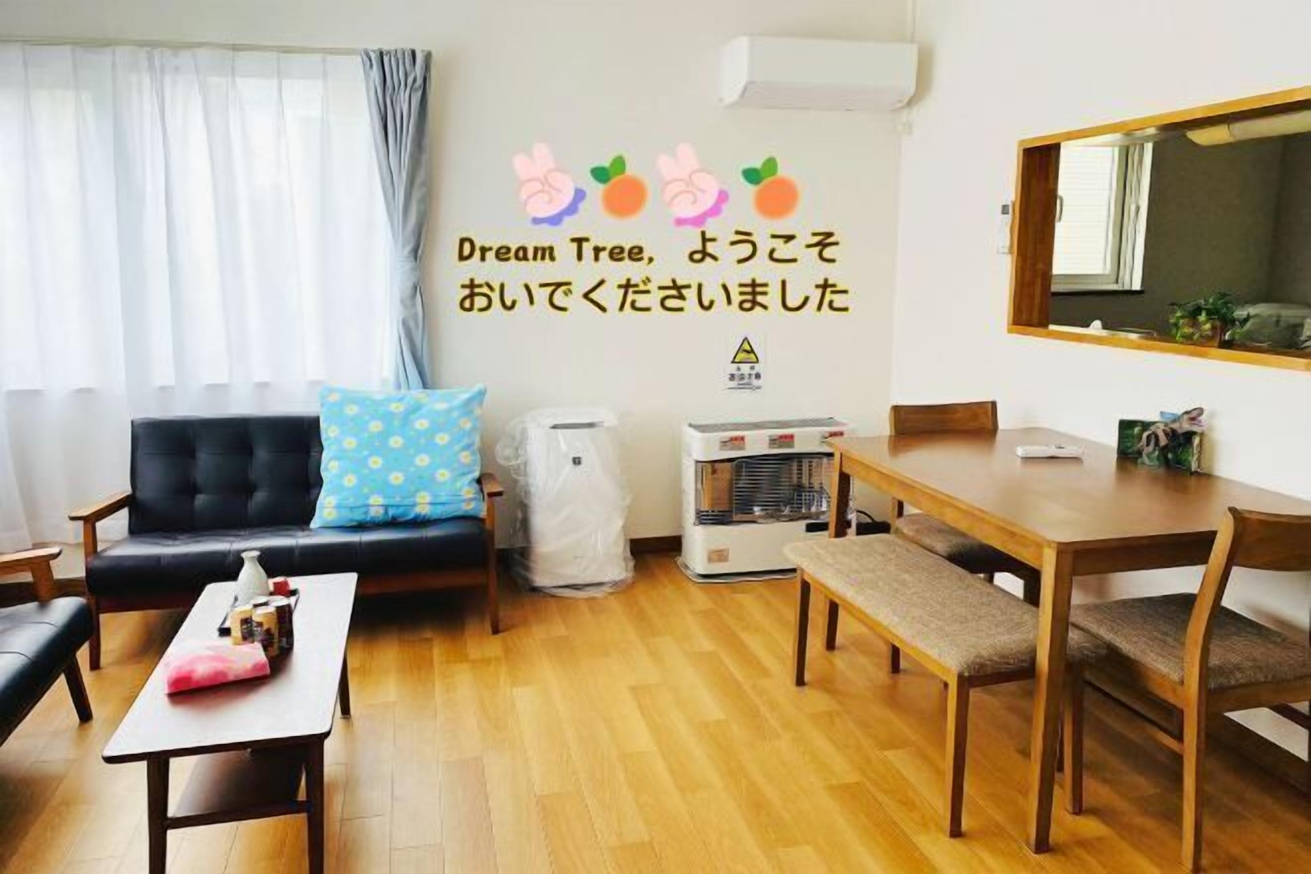 A living room with a sofa, a coffee table, a dining table with chairs, and a wall-mounted air conditioner.