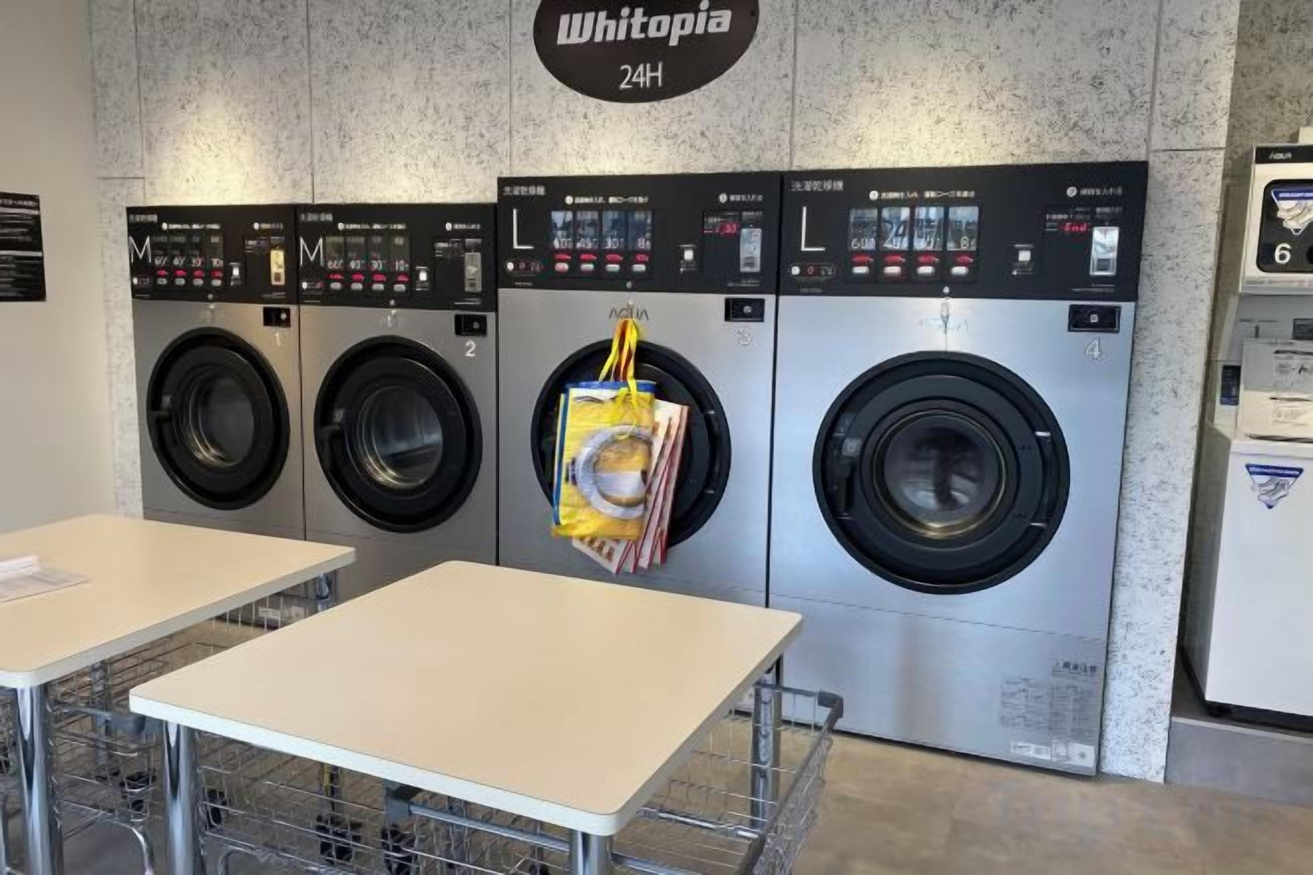Een wasserette met drie wasmachines en drogers, een bord met 24-uurs service en een tafel met een mand.