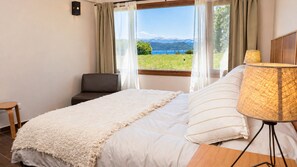 A bedroom with a bed, a chair, a lamp, and a view of the outdoors. - Mascardi Ground Floor Lake Front (Dina Huapi)