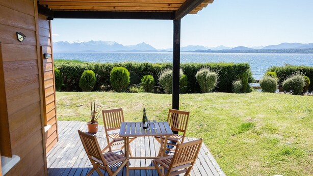 A wooden deck with a table and chairs, overlooking a lake with mountains in the background. - Mascardi Ground Floor Lake Front (Dina Huapi)