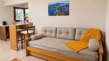 A cozy room with a sofa, a dining table, and a chair. There is a window with a view of a lake and mountains.