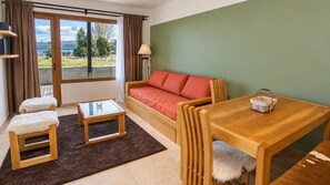 A room with a sofa, a table, a chair, a small stool, and a window with curtains. - Mascardi Fivefold Ground Floor LakeView Dina Huapi (Dina Huapi)