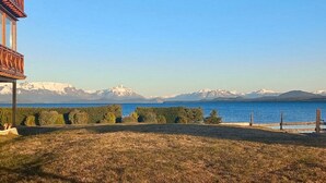 A view of a lake with mountains in the background, a wooden deck, and a grassy area in the foreground. - Mascardi Fivefold Ground Floor LakeView Dina Huapi (Dina Huapi)