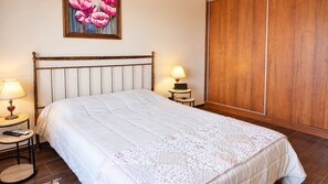 A neatly made bed with a white duvet and a floral-patterned blanket, two bedside tables with lamps, a wooden headboard, and a wooden wardrobe.