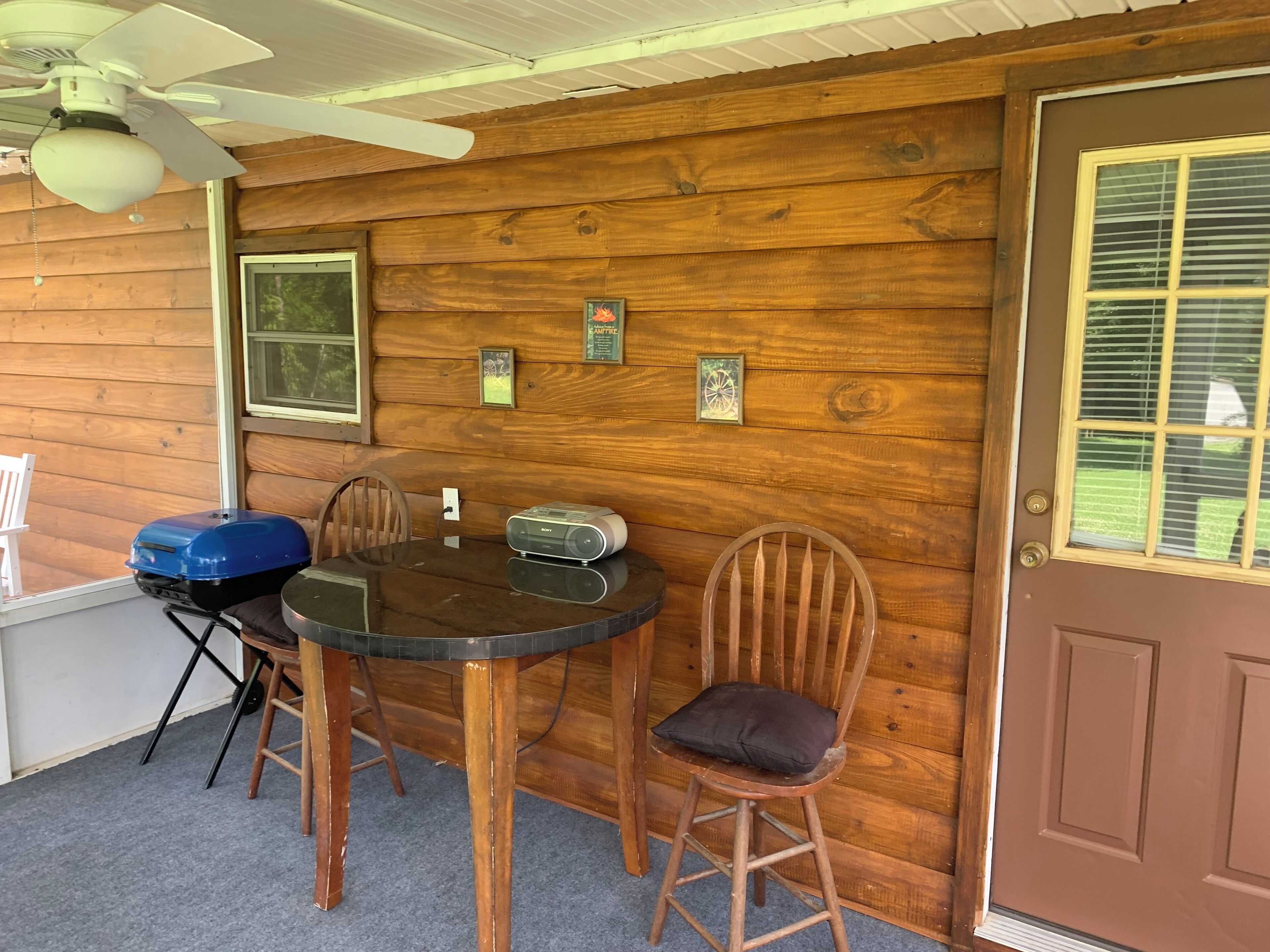 Interior d'una cabana de fusta amb una taula de dinar, cadires, un ventilador de sostre i una porta amb una finestra.