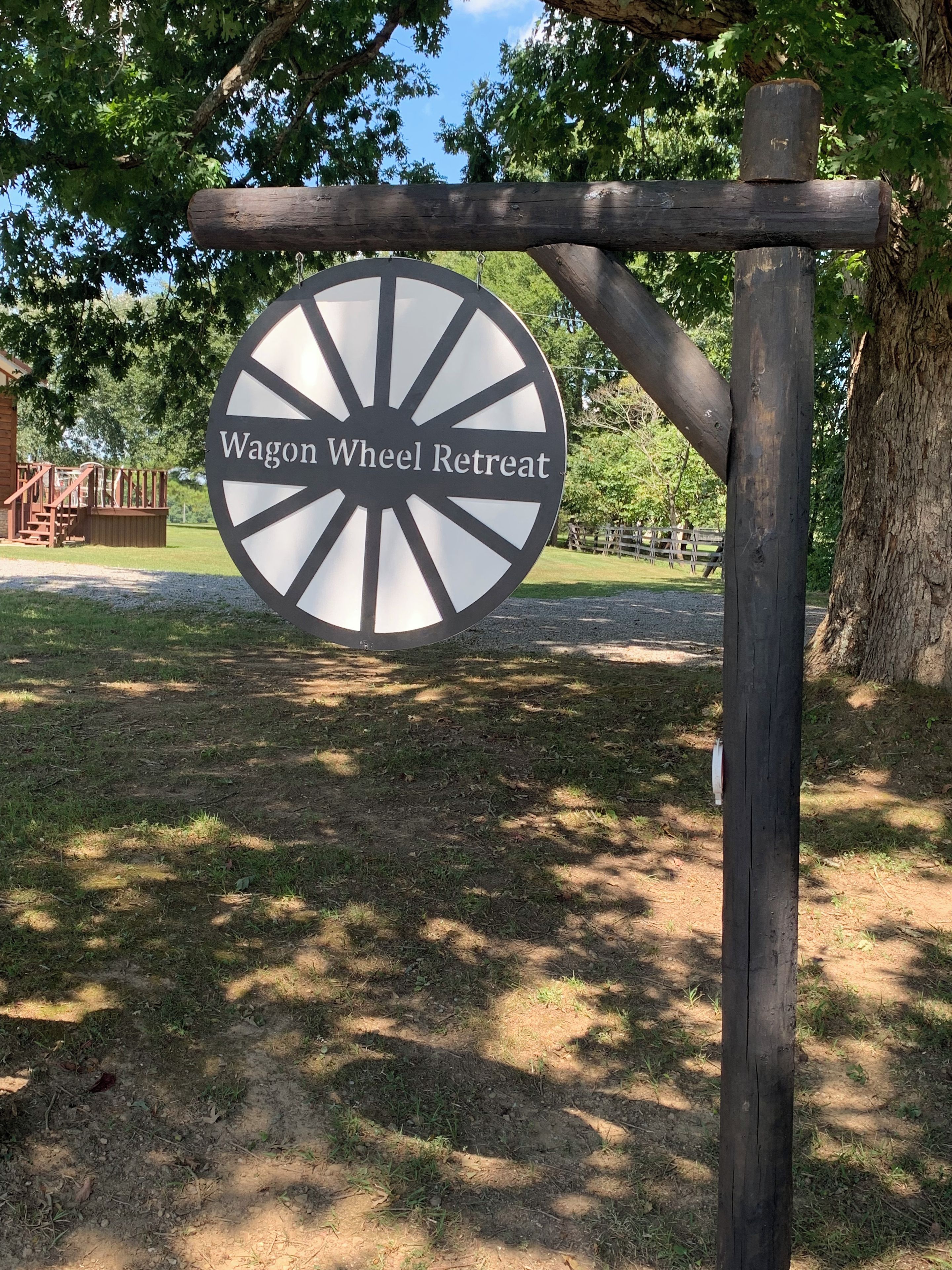 Une enseigne pour le Wagon Wheel Retreat, avec un poteau en bois rustique et un panneau circulaire à rayons.