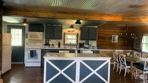 A kitchen with dark wooden cabinets, a white island, and a dining area with white chairs. - Wagon Wheel Retreat, Pulaski, TN 3 Bedroom home in the Country. 20% off/weekly (Pulaski)