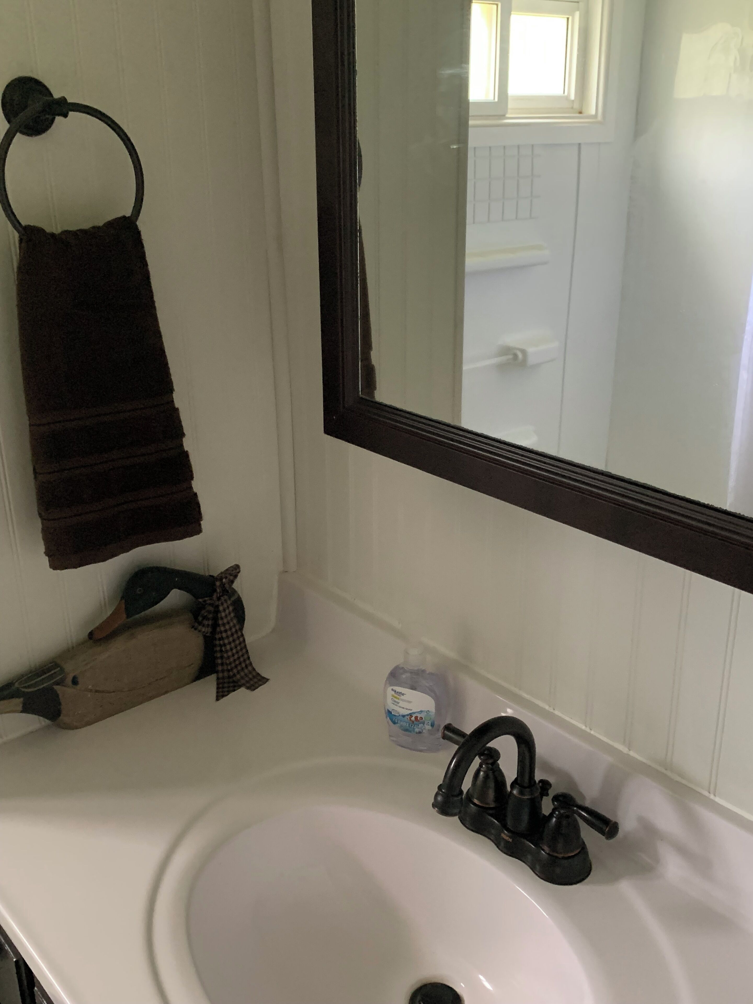 A bathroom with a white sink, a dark faucet, a towel rack with a brown towel, a duck decoration, and a bottle of hand soap.
