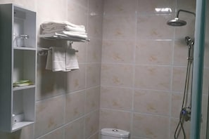 A shower area with a toilet, a shelf with folded towels, and a showerhead. - Wusheng Chengbei Business Hotel (Wusheng)