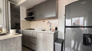 Een moderne keuken met grijze kastjes, een roestvrijstalen koelkast, een magnetron en een spoelbak met een kraan.