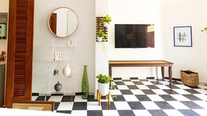 Une pièce avec un sol à carreaux, un banc en bois, un miroir rond et un téléviseur fixé au mur.