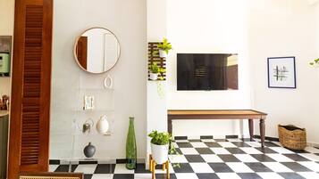 Een kamer met een geruit vloertje, een houten bankje, een ronde spiegel en een aan de muur bevestigde televisie.
