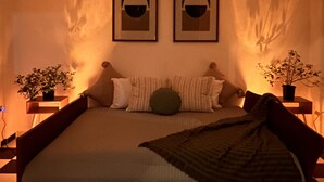 Une chambre à coucher avec un lit, deux tableaux encadrés accrochés au mur et deux plantes en pot posées sur des tables de chevet.