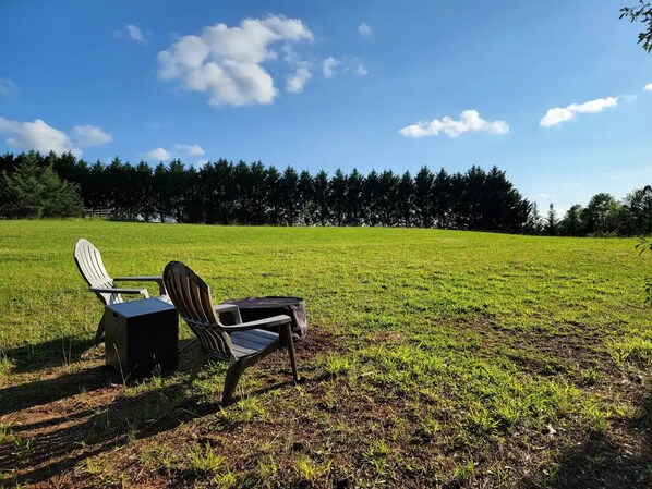 Ein Stuhl und ein Tisch in einer offenen, grasbewachsenen Wiese, im Hintergrund ein Wald.