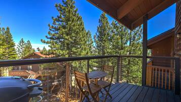 A wooden deck with a grill, a table, and chairs, overlooking a forested area.