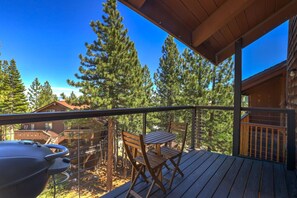 Une terrasse en bois avec un barbecue, une table et des chaises, donnant sur une zone boisée.