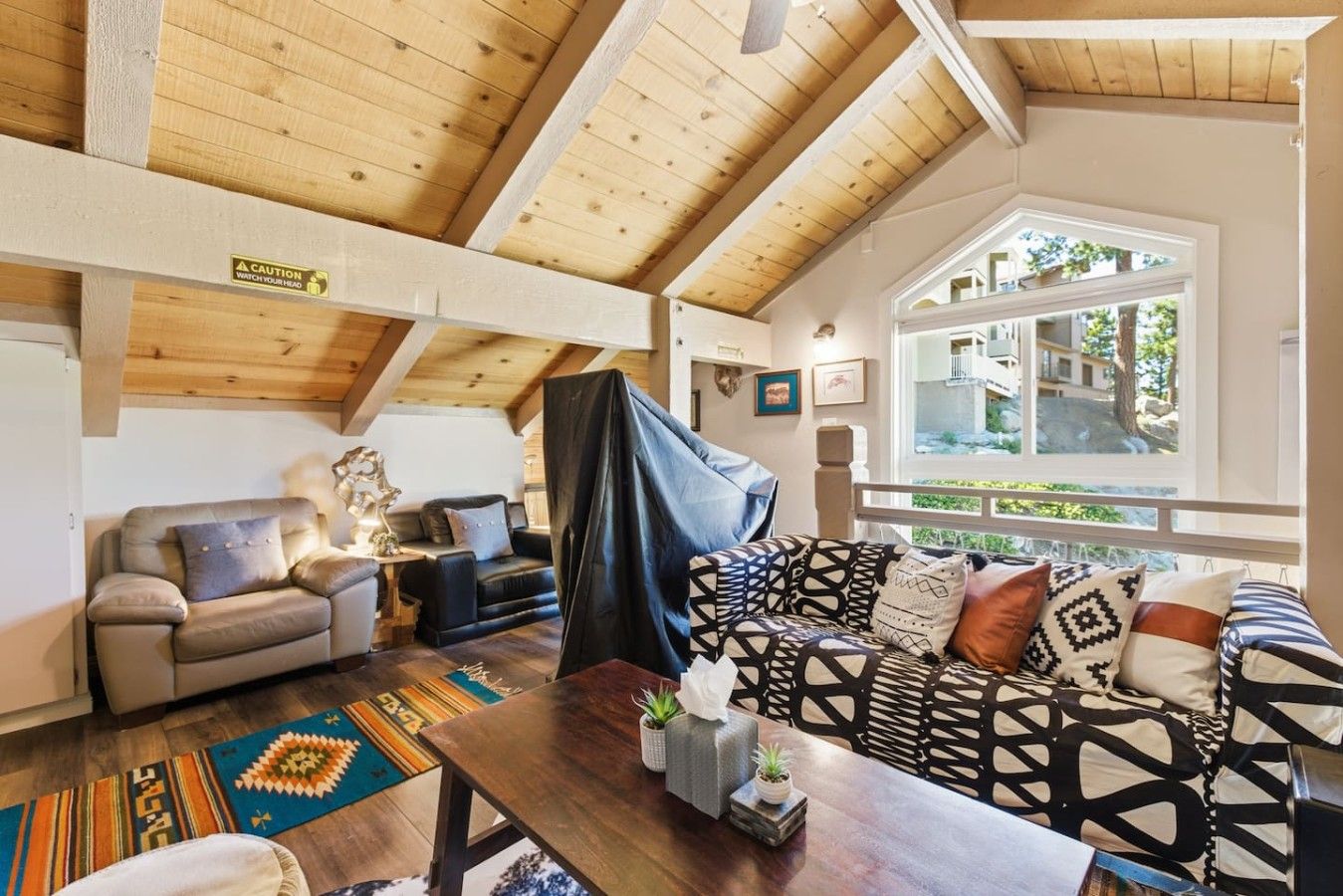 A cozy loft-style living room with high ceilings, a large window, and a mix of modern and traditional furnishings.