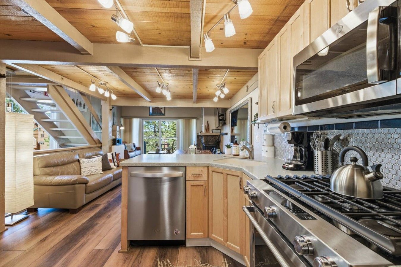 A modern kitchen with a central island, stainless steel appliances, and a wooden ceiling.