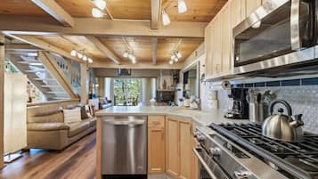 A modern kitchen with a central island, stainless steel appliances, and a wooden ceiling.