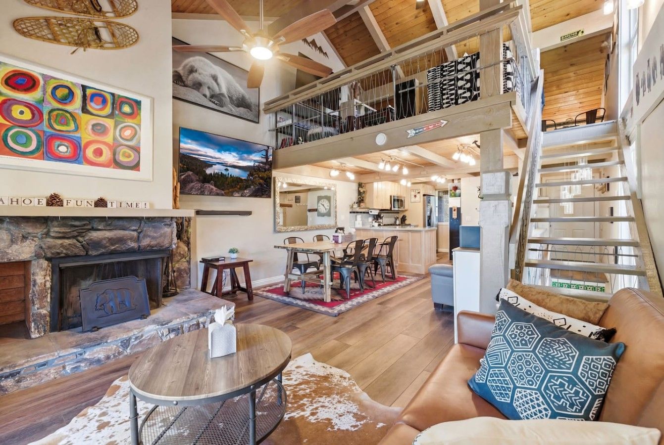A spacious living area with a fireplace, dining table, and a staircase leading to an upper level.