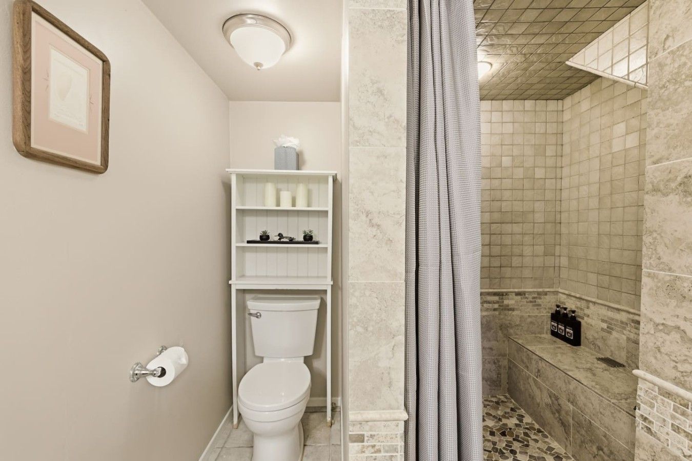 A bathroom with a toilet, a shelf with toiletries, and a shower area with a tiled wall.