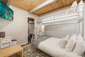 Une chambre avec un lit superposé, une échelle, une table de chevet, un petit bureau et une étagère fixée au mur.