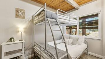 Une chambre avec un lit superposé, une fenêtre, une lampe de chevet et une petite étagère sur laquelle est posé un panneau.