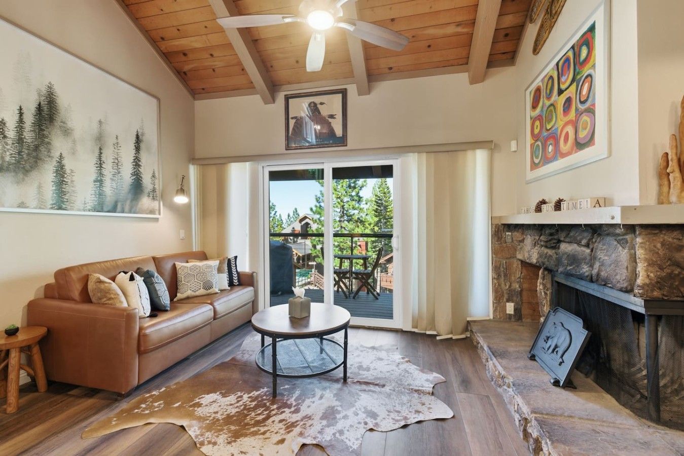 A living room with a leather sofa, a round coffee table, a fireplace, and a large painting of trees.