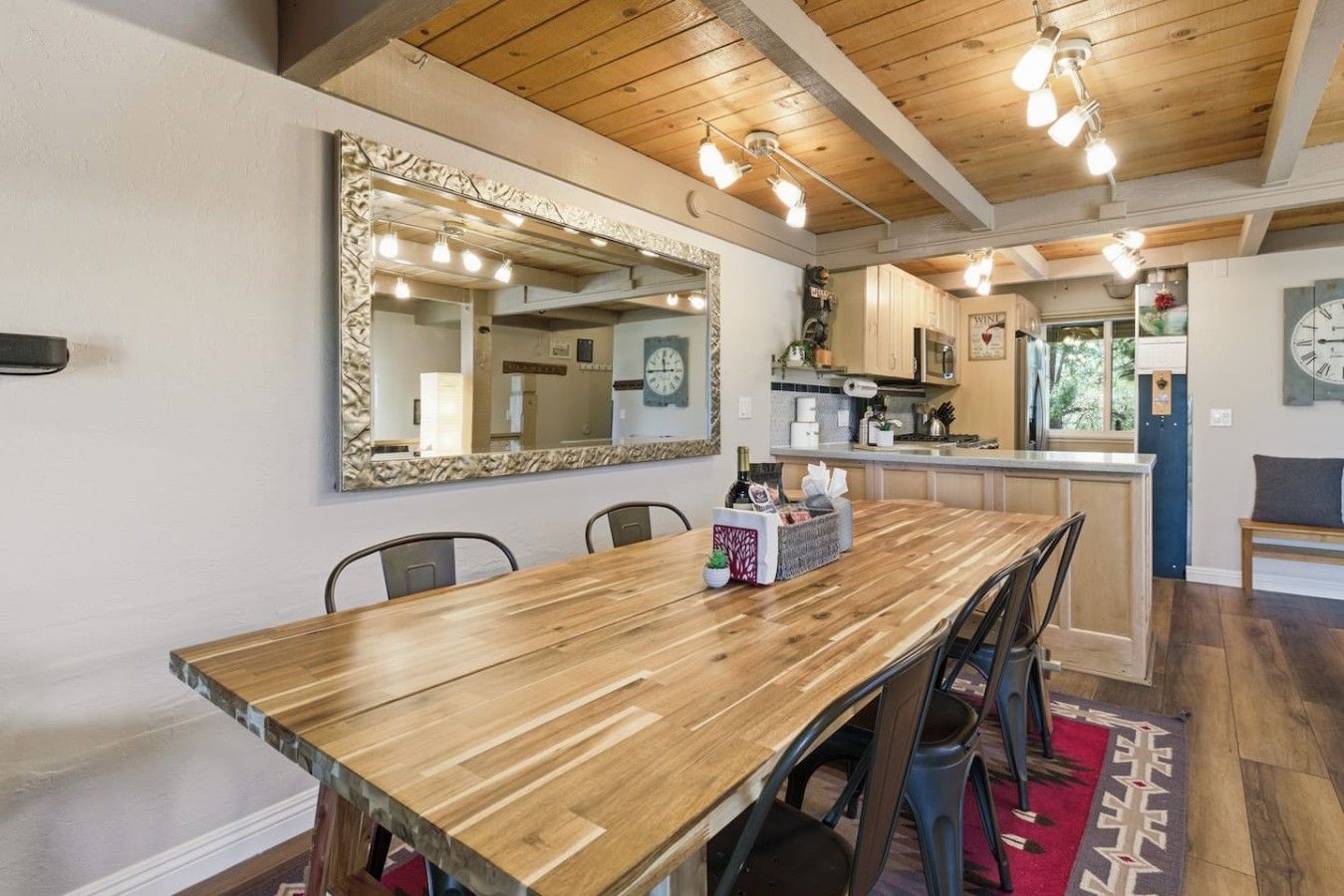 Een eetgedeelte met een houten tafel, stoelen, een grote spiegel en een keuken op de achtergrond.